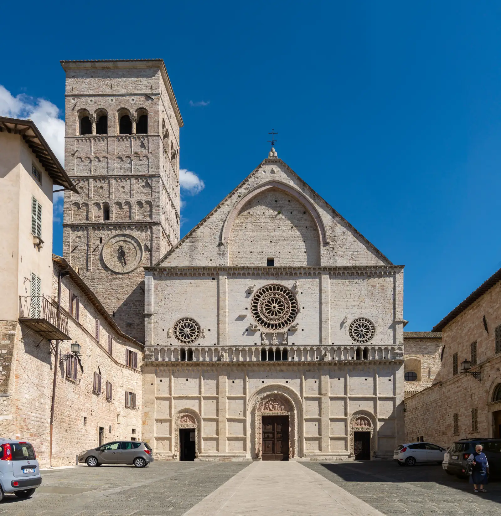 The Romanesque facade of the Cathedral of San Rufino in Assisi, with its bell tower and three rose windows.