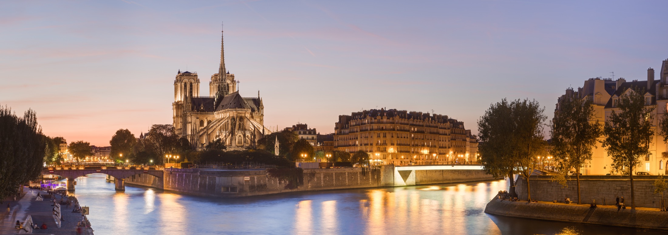 Notre-Dame Cathedral and the Île de la Cité seen from the Seine at dusk.