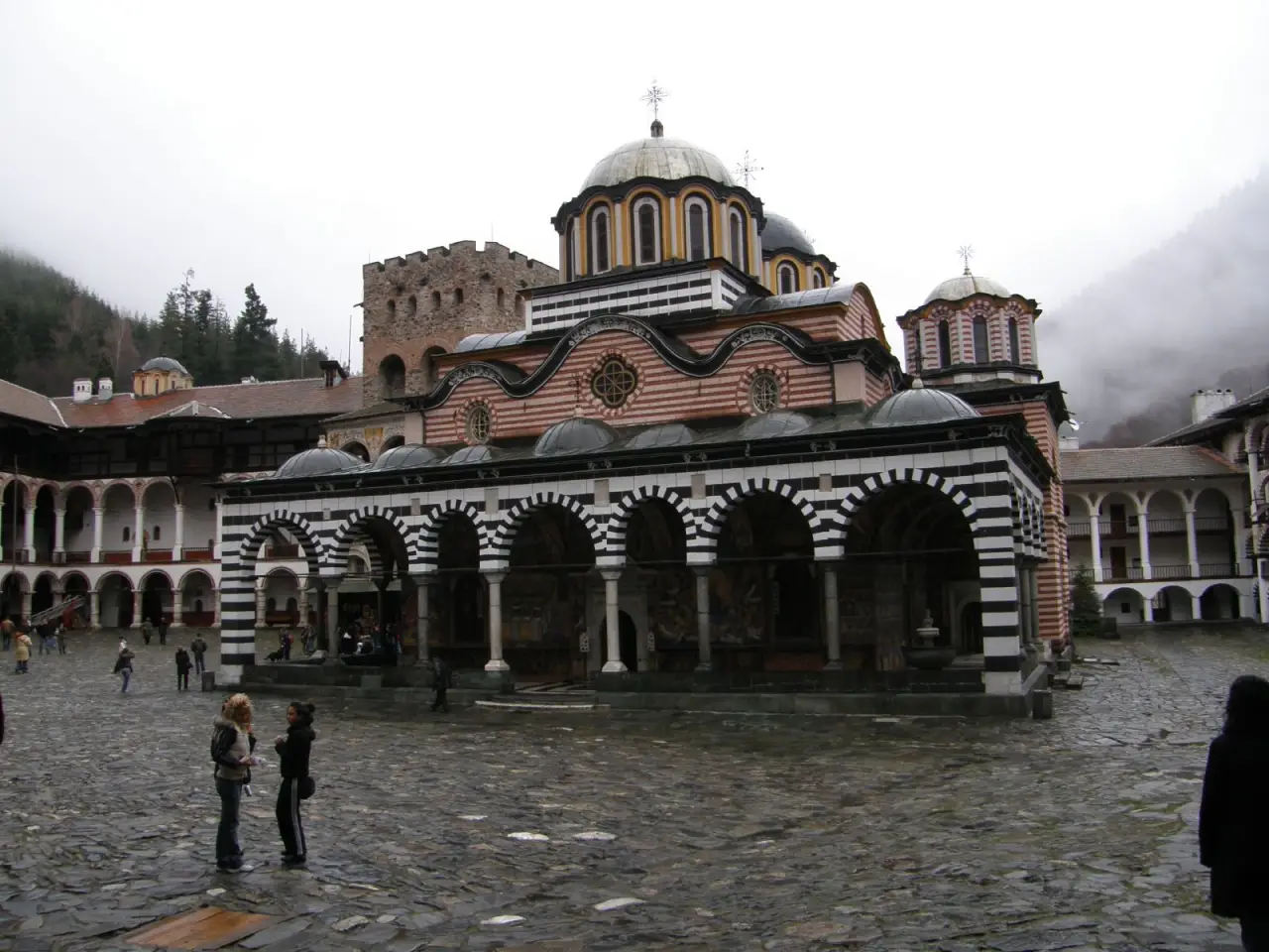 Rila Monastery's striped arcaded courtyard church and stone defensive tower beneath the Rila Mountains.