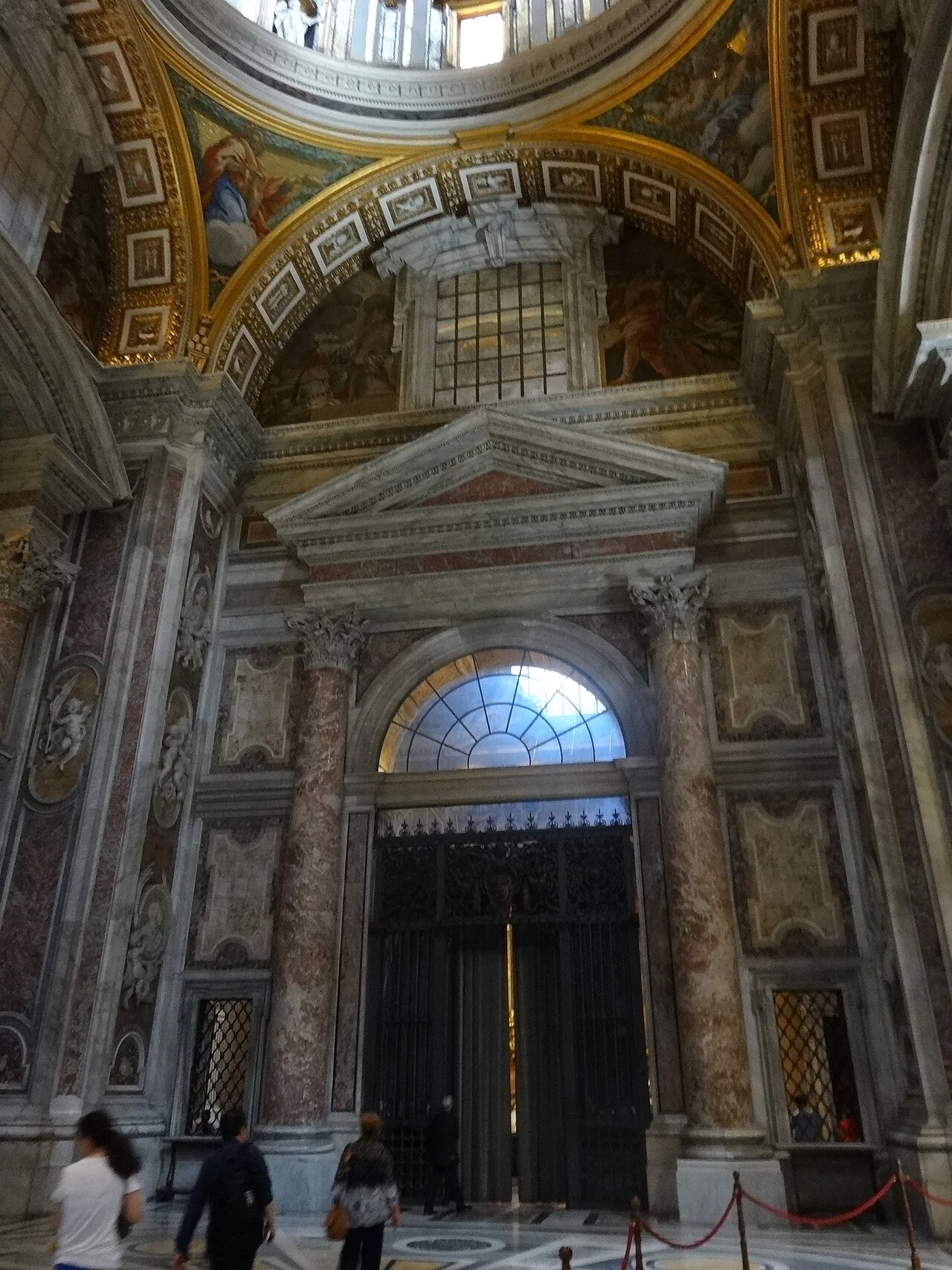 A marble side portal and gilded vault inside St. Peter's Basilica.