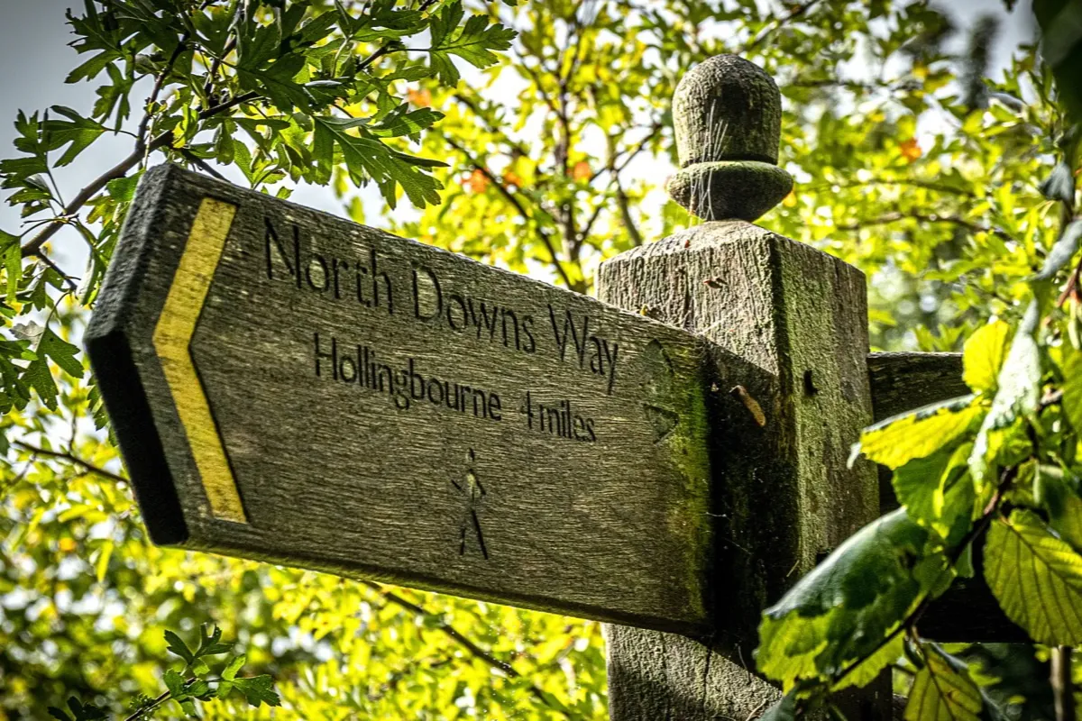 A weathered North Downs Way fingerpost with a walker symbol on the old pilgrims' route to Canterbury.