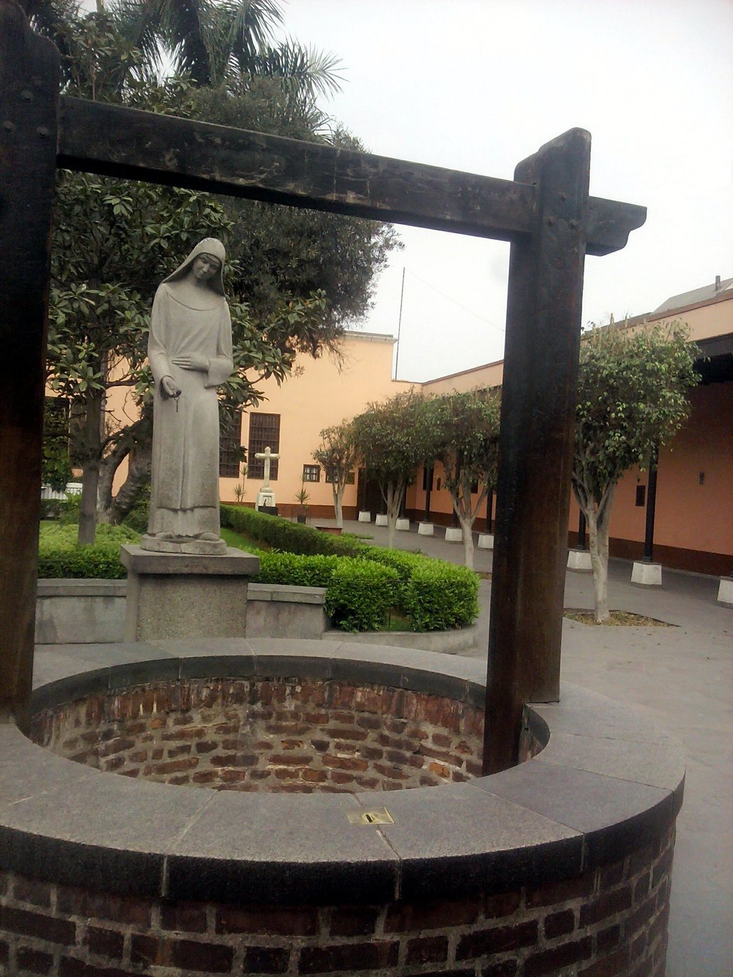 The brick well in the garden of the Sanctuary of Saint Rose of Lima, with a statue of the saint behind it.