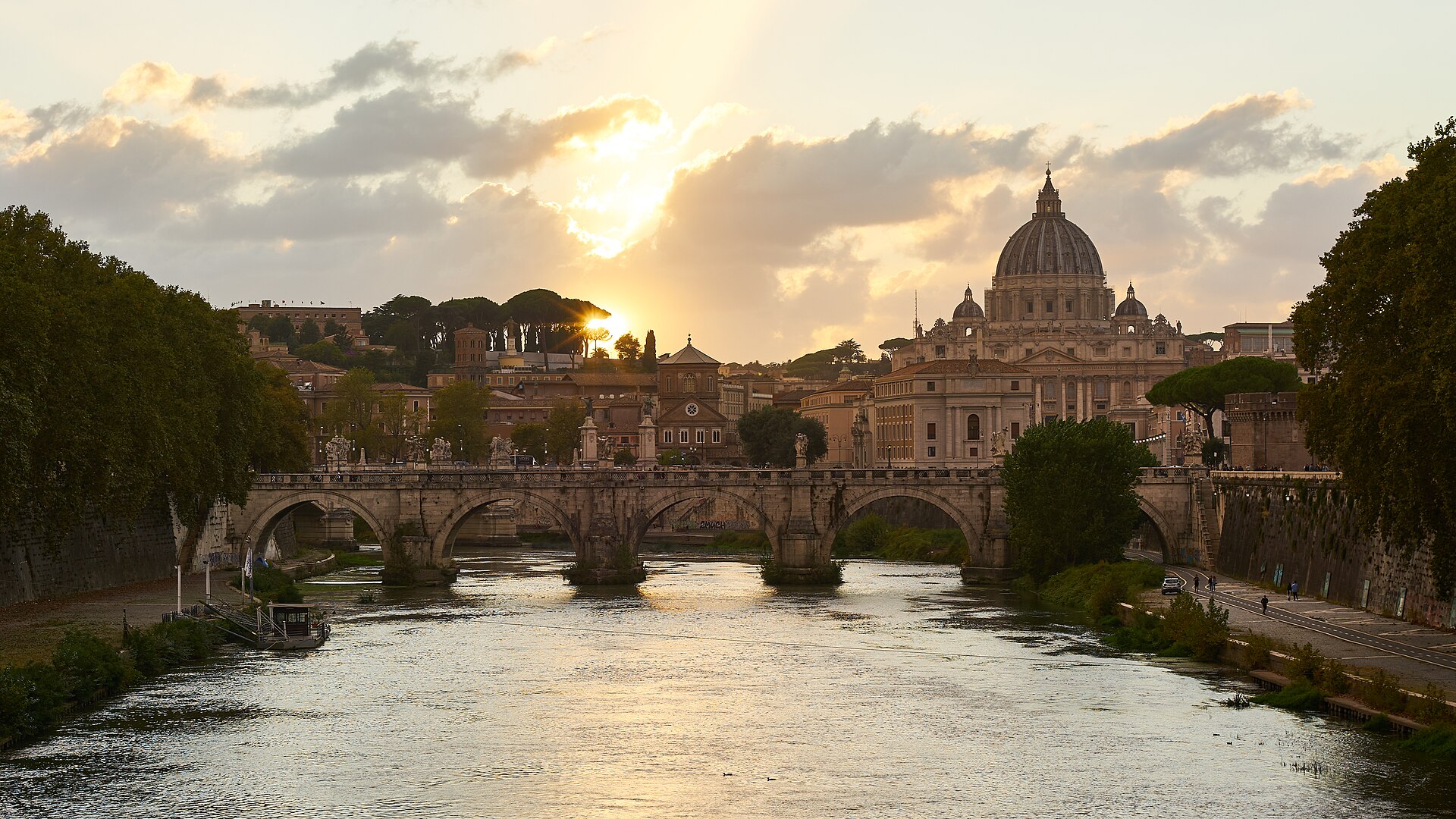 St. Peter's Basilica and its dome in golden sunset light across the Tiber, with Ponte Sant'Angelo in the foreground
