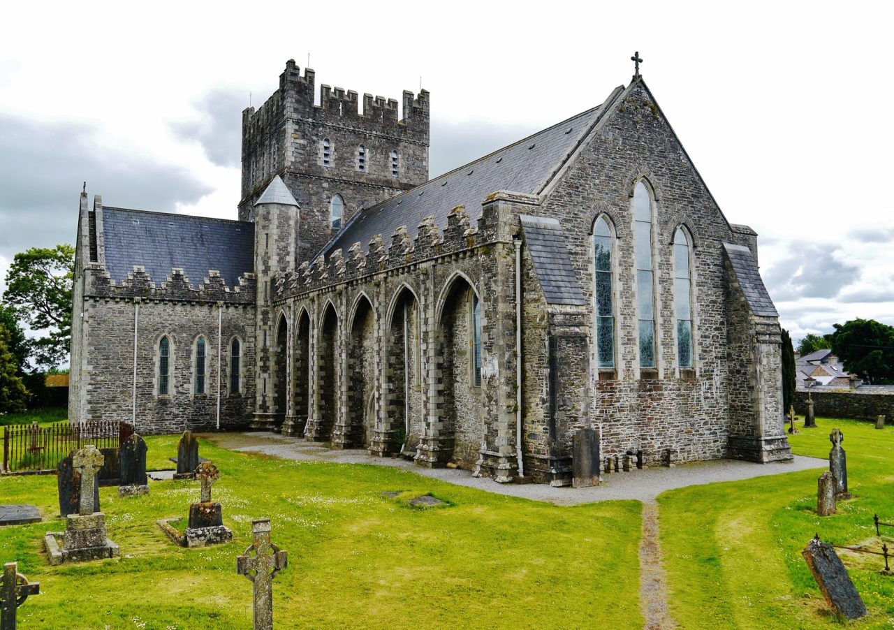 Saint Brigid's Cathedral in Kildare seen from the north west, its battlemented tower and stepped buttresses rising above the surrounding graveyard.