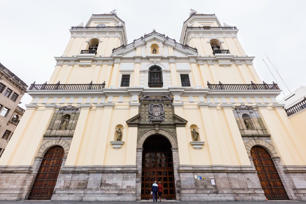 The cream and yellow baroque facade of the Church of San Pedro in Lima, with its twin bell towers and carved central portal.