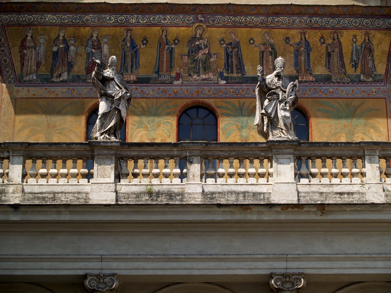The gold facade mosaic of Santa Maria in Trastevere in Rome, showing the Virgin enthroned among a procession of women bearing lamps, above a baroque balustrade.
