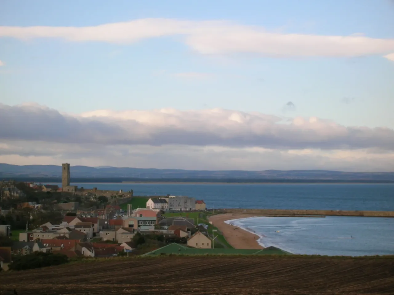St Andrews seen across fields toward the bay, with St Rule's Tower rising beside the cathedral ruins.