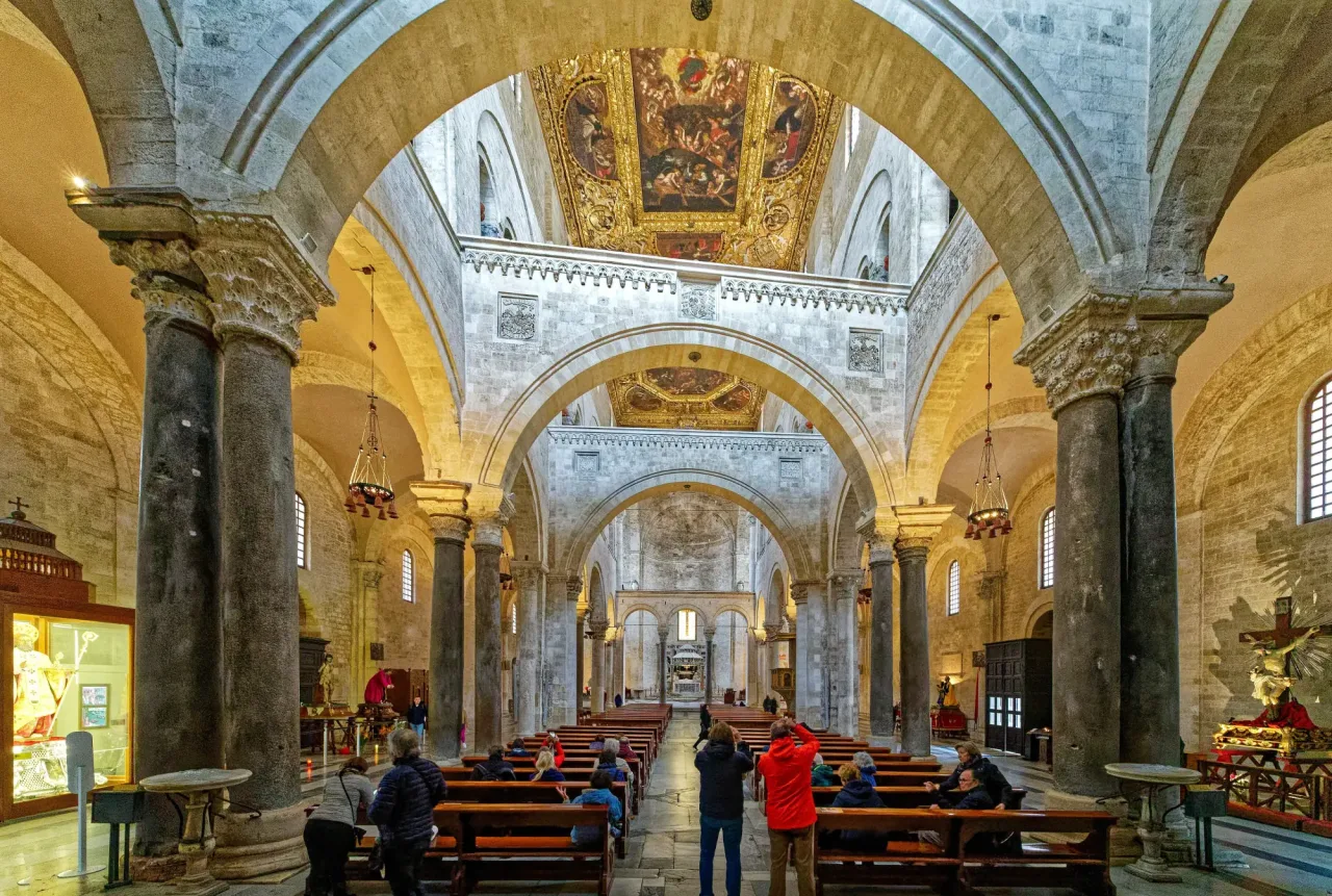 The nave of the Basilica di San Nicola in Bari looking toward the altar, with tall columns, three great transverse arches crossing the nave, and a gilded and painted coffered ceiling above.