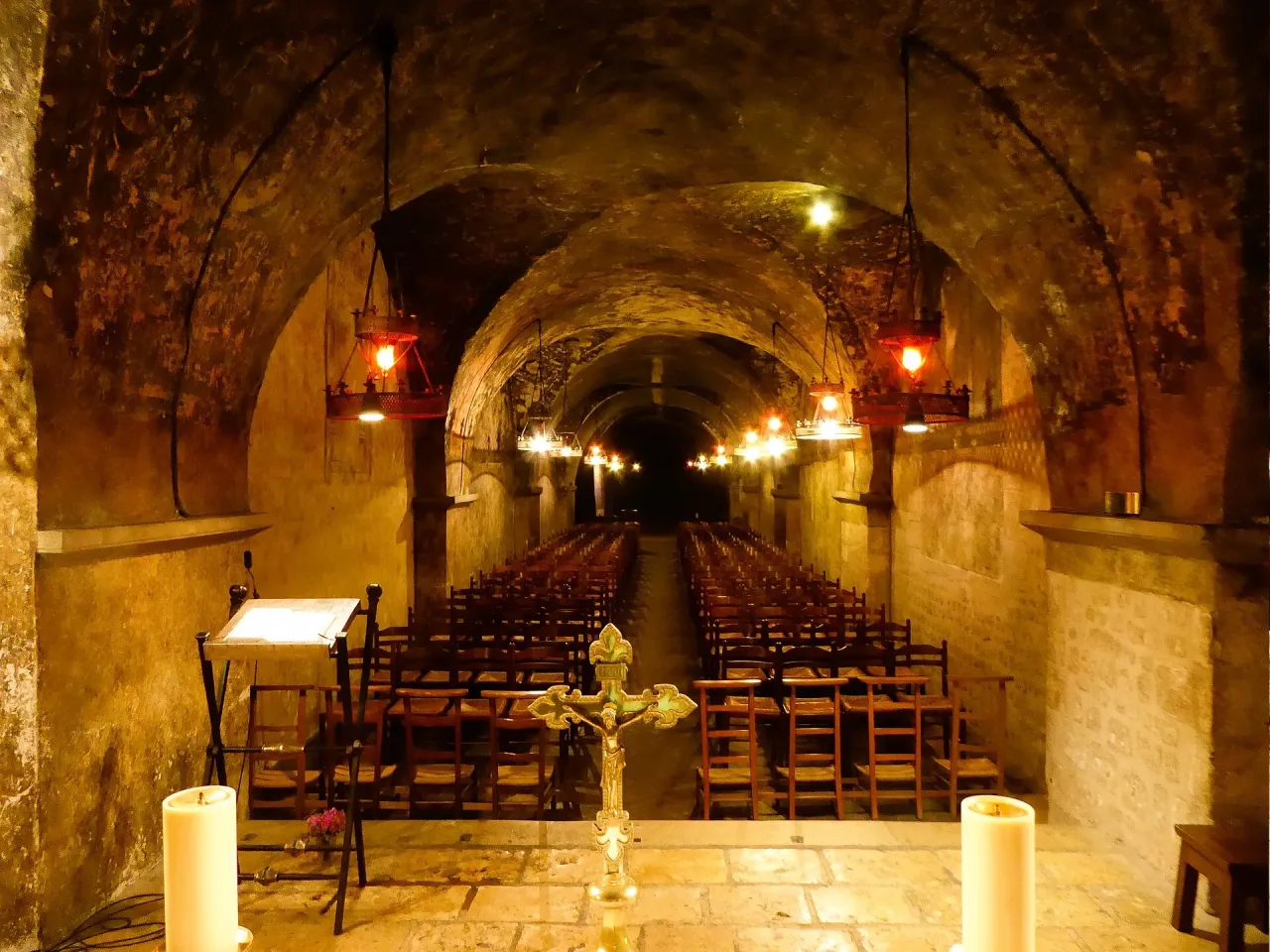 The chapel of Notre-Dame de Sous-Terre in the crypt of Chartres Cathedral, its barrel-vaulted gallery lit by hanging lamps and set with rows of chairs.
