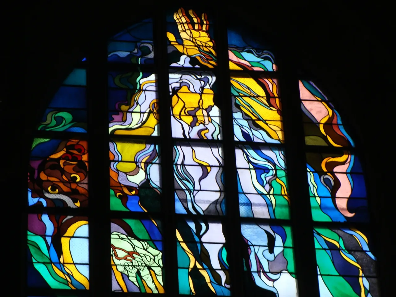 Stanisław Wyspiański's stained glass window of God the Father above the choir of the Franciscan basilica in Kraków, in swirling blue, green and gold.