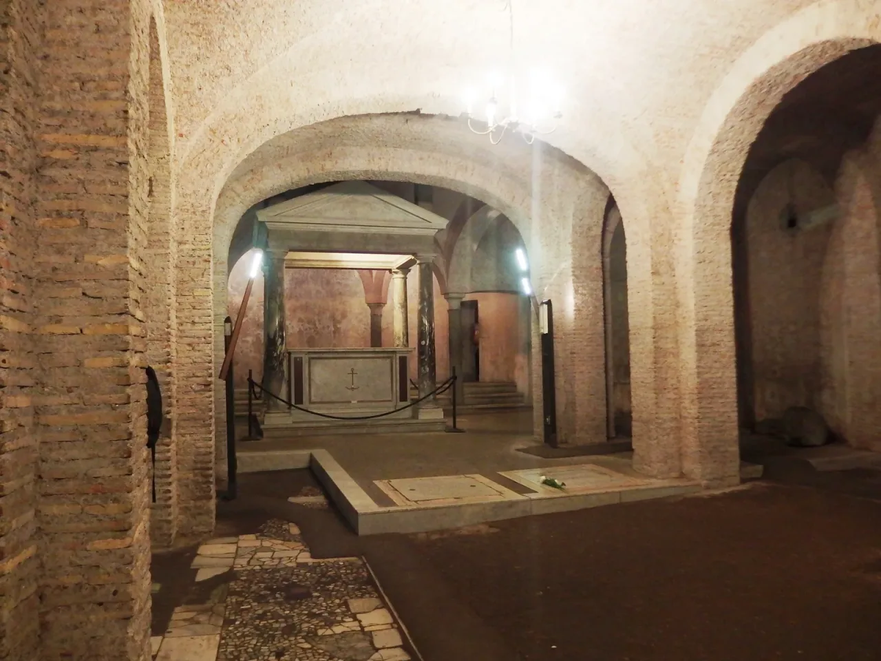 The fourth century lower basilica beneath San Clemente in Rome, a brick and stone aisle with faded wall painting.