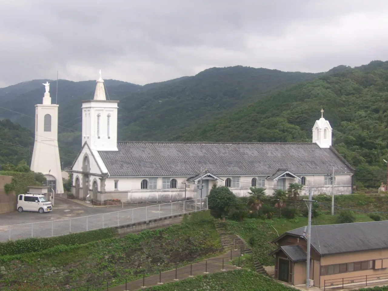 The long low roof and white bell tower of Shitsu Church below forested ridges on the Sotome coast.