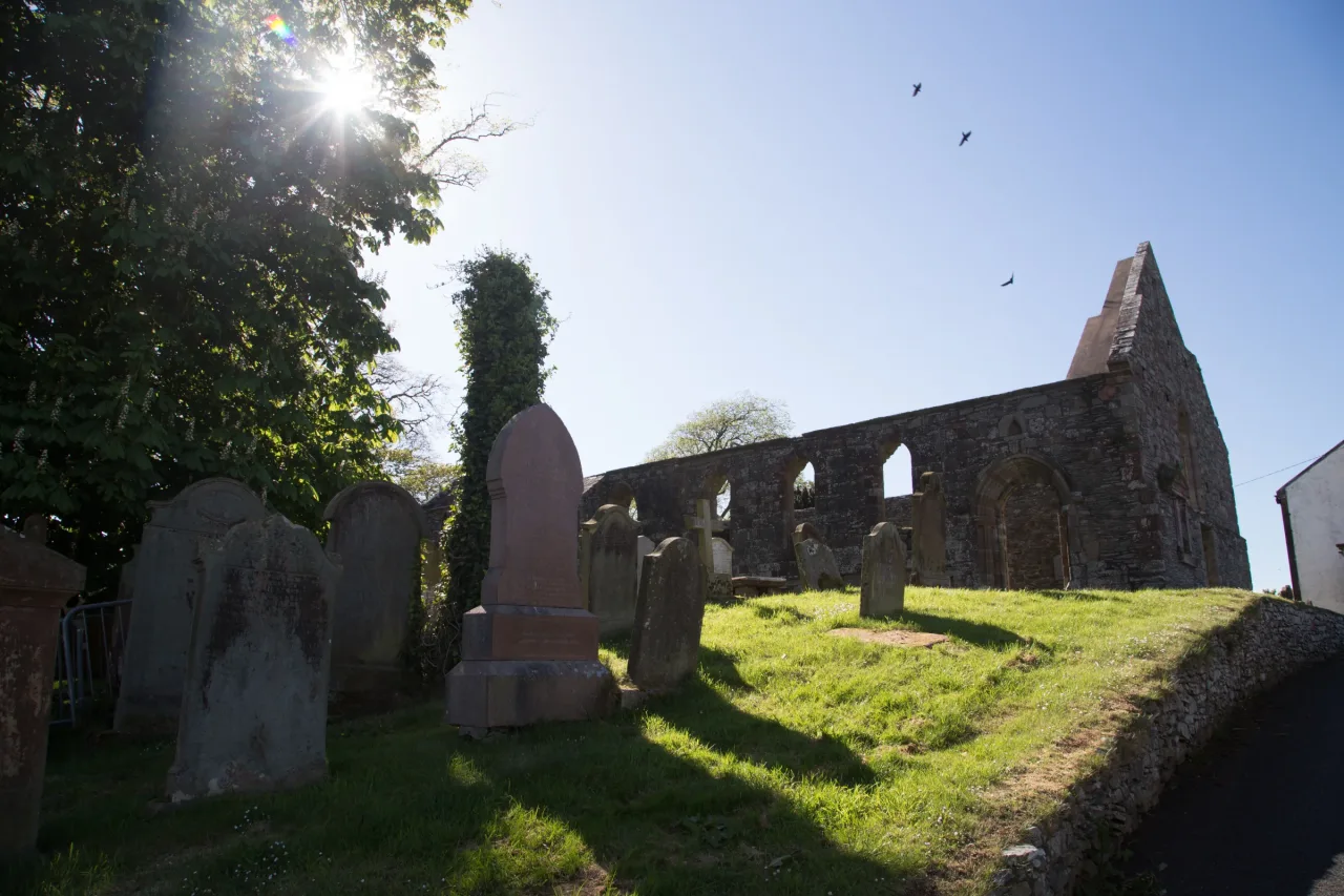 The roofless west end of Whithorn Priory rising above an old graveyard in strong morning light.