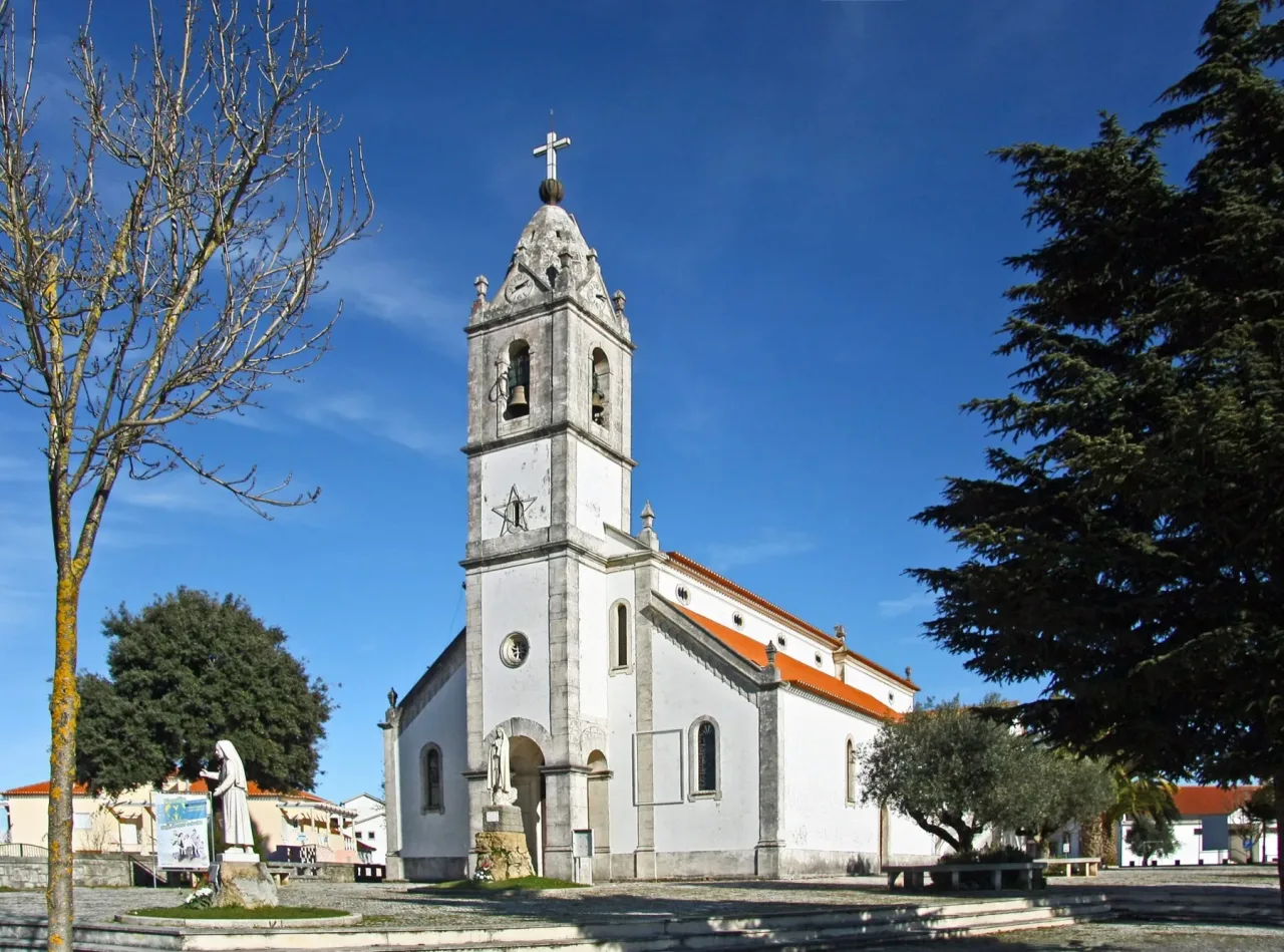 The whitewashed parish church of Fátima with its stone bell tower and red tiled roof, seen across the square in front of it.