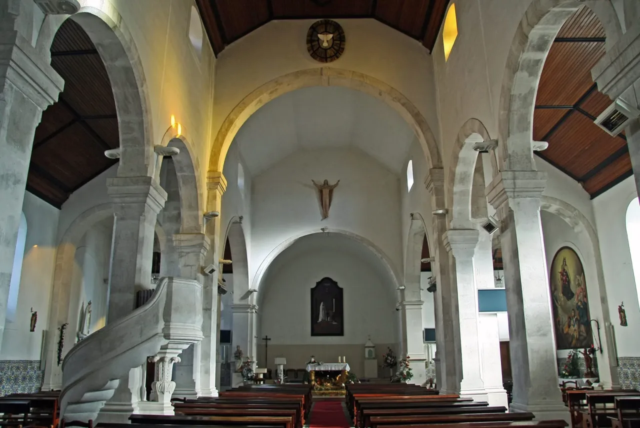 The three-aisled interior of the parish church of Fátima, with stone arches, a wooden roof, and a stone pulpit on the left.