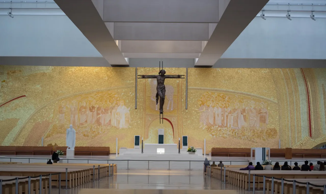 The sanctuary wall of the Basilica of the Most Holy Trinity at Fatima, a wide gold mosaic behind the altar with a bronze crucifix suspended above it.