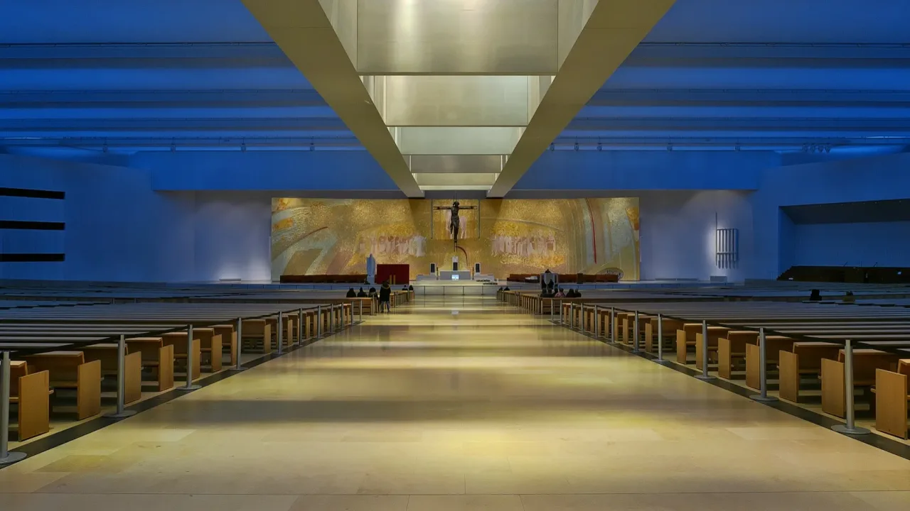 The nave of the Basilica of the Most Holy Trinity at Fatima looking toward the altar, with long banks of benches under a low ceiling.