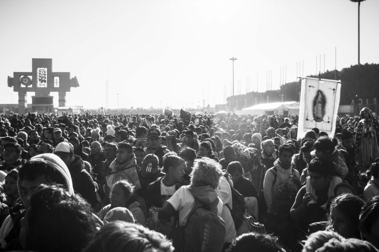 A crowd of pilgrims filling the plaza of the Guadalupe sanctuary with a Guadalupe banner raised.