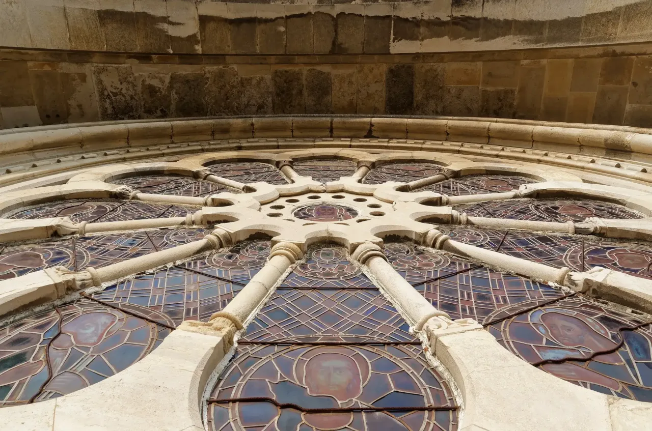 The rose window of Lisbon Cathedral seen from inside the nave, its stained glass set within radiating stone tracery.
