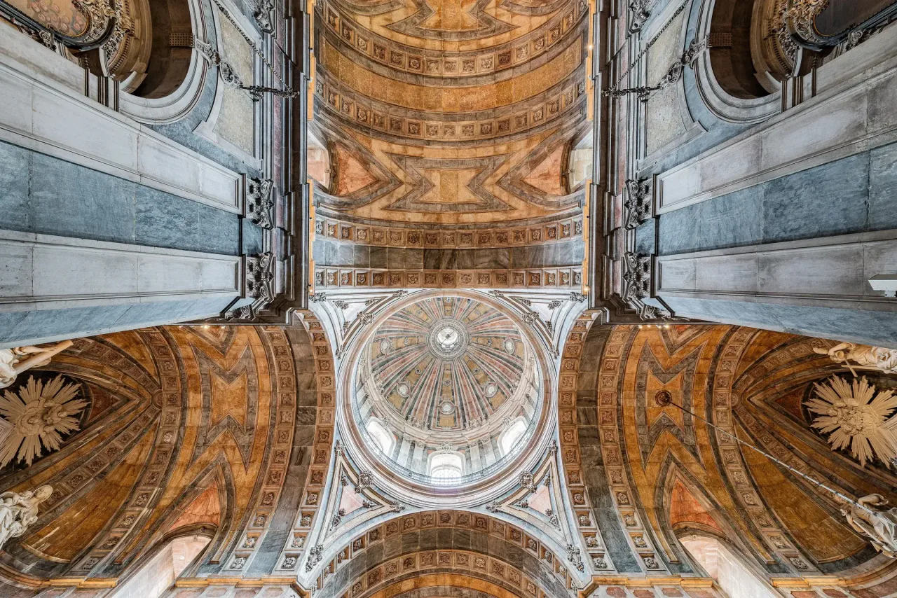 Looking up into the dome of the Estrela Basilica, its coffered vault and arches faced in patterned pink, grey and cream marble.