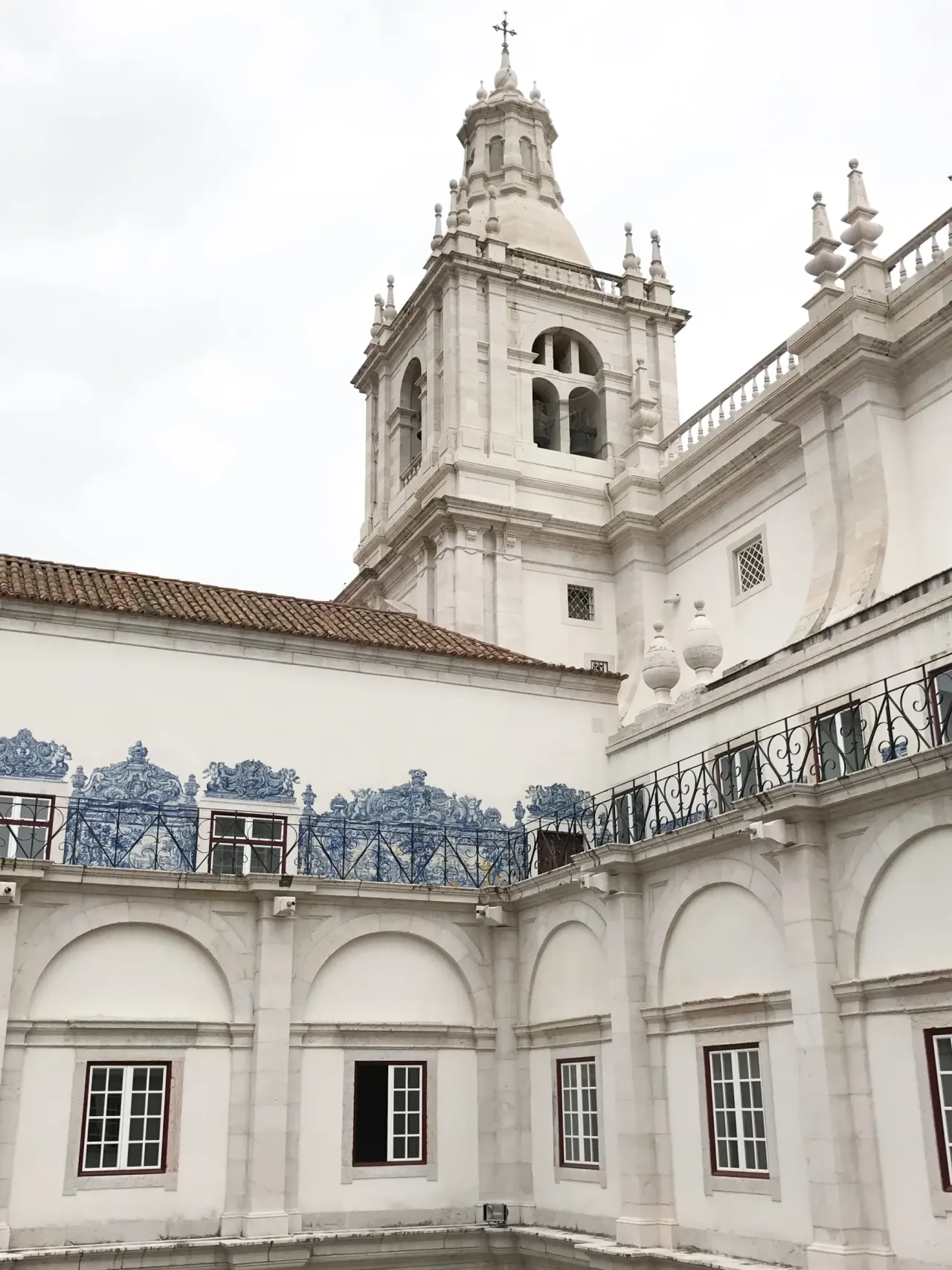 A bell tower and dome of São Vicente de Fora rising above the monastery's white walls and azulejo-panelled upper terrace.