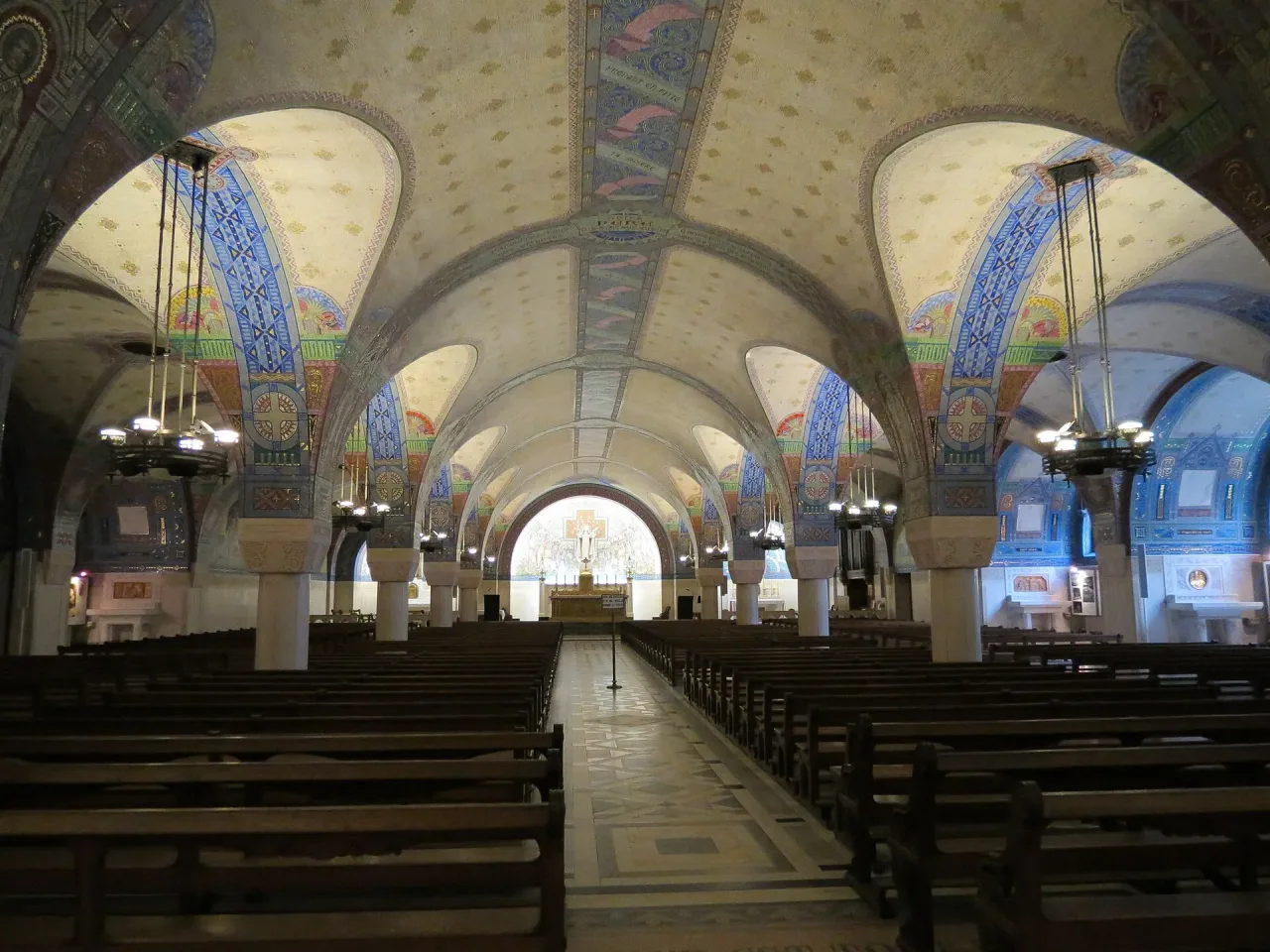 The crypt of the Basilica of Sainte-Thérèse in Lisieux, its marble piers and mosaic walls running toward the altar.