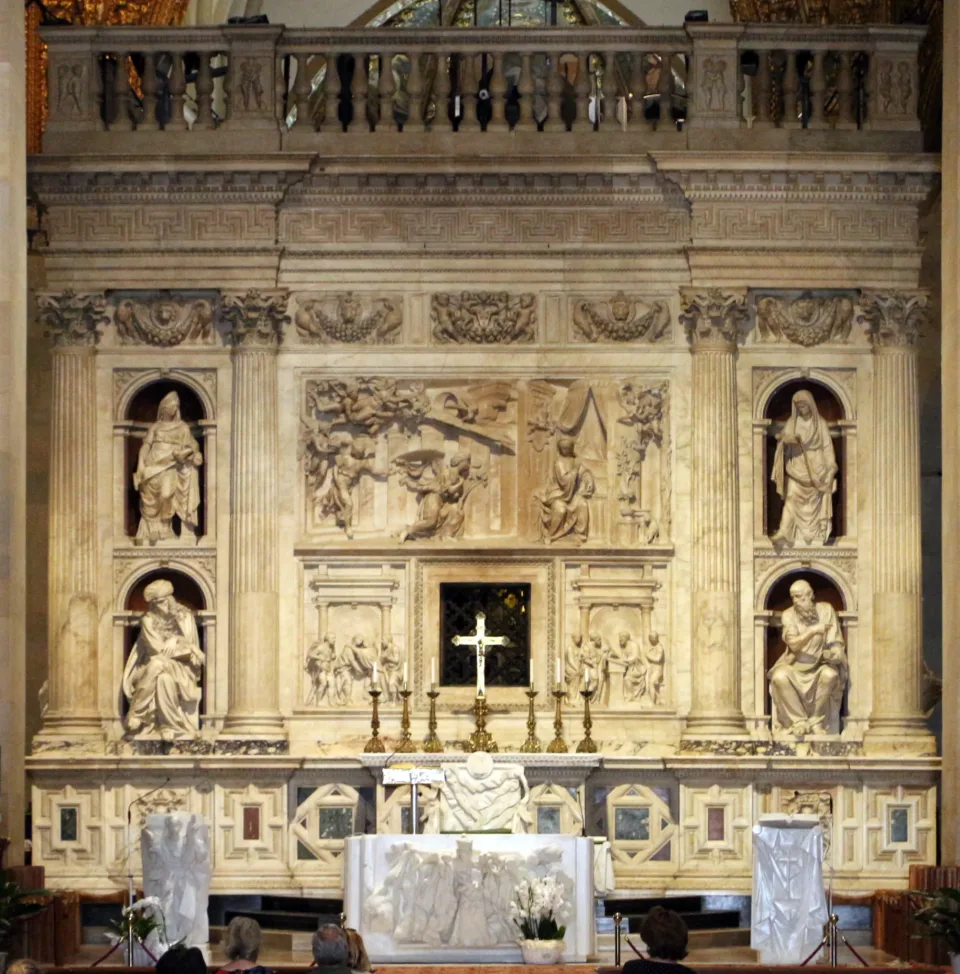 The west face of the carved marble enclosure seen from the nave, with a large Annunciation relief at its center, prophets and sibyls seated in niches, and an altar in front.