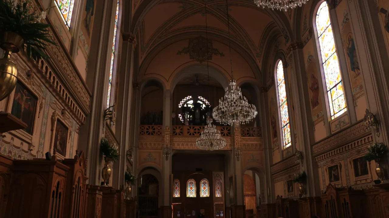 The nave of the Sagrada Familia parish church in Colonia Roma seen towards the organ gallery, with painted vaults, tall stained-glass windows and cut-glass chandeliers.