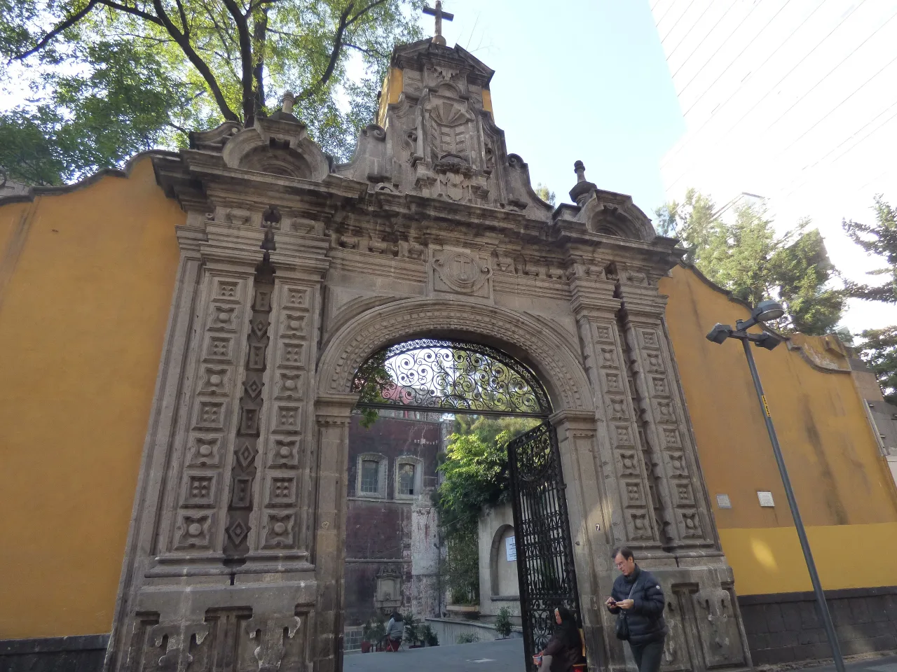 The carved stone gateway into the atrium of the church of San Francisco on Calle Madero, an ornate arch set into a plain ochre wall with the church front visible through the ironwork.