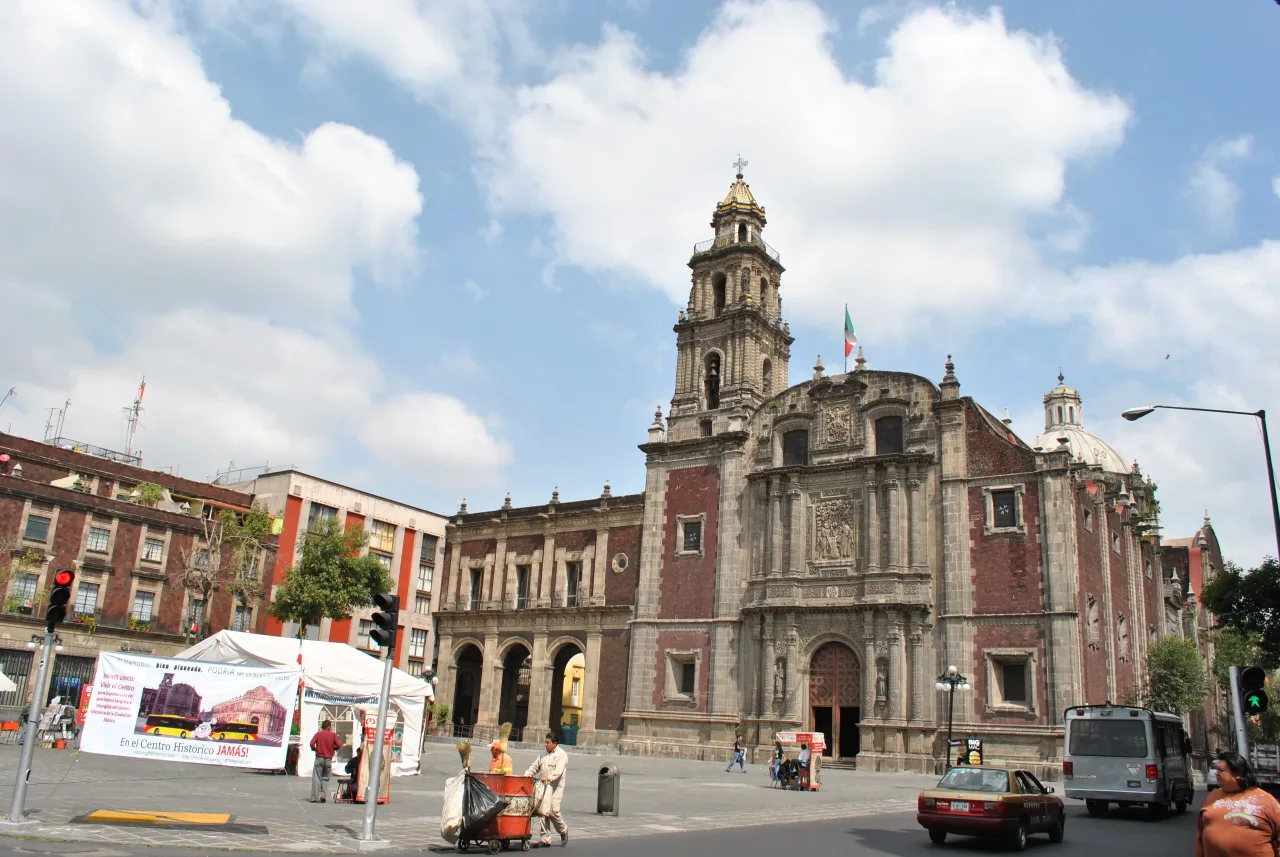 The eighteenth-century baroque front of the church of Santo Domingo in Mexico City, its single bell tower rising beside a carved stone portal set in dark red tezontle.