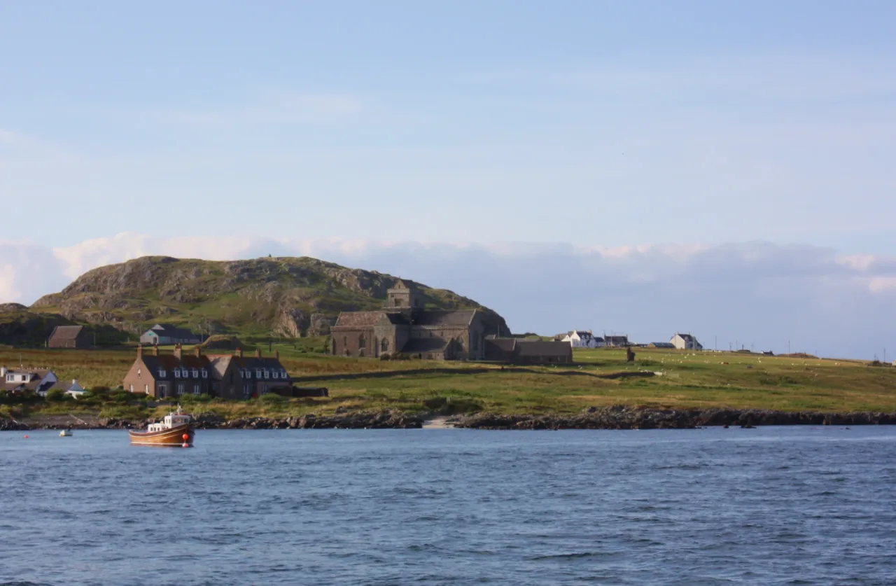 Iona Abbey standing beyond the Sound of Iona, with a small boat on the water in the foreground.