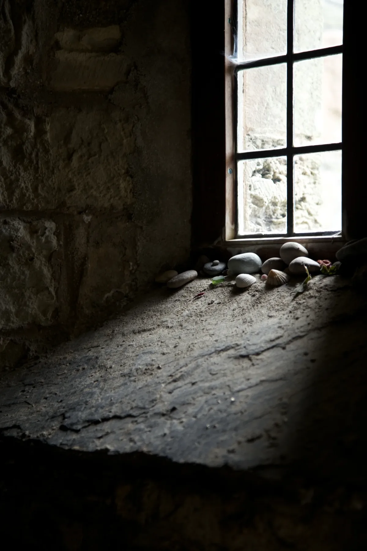 Pebbles and shells left in prayer on the deep stone window ledge inside Saint Columba's shrine on Iona.