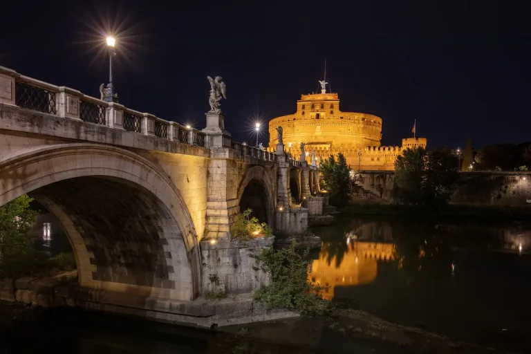 Castel Sant'Angelo and the Ponte Sant'Angelo lit at night above the Tiber in Rome.
