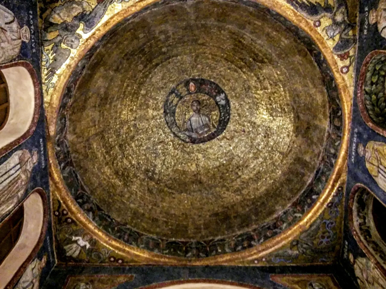 The gold mosaic vault of the Sacello di San Vittore in Ciel d'Oro, with a bust of Saint Victor in a wreath at the center and named figures of saints on the walls at the corners.