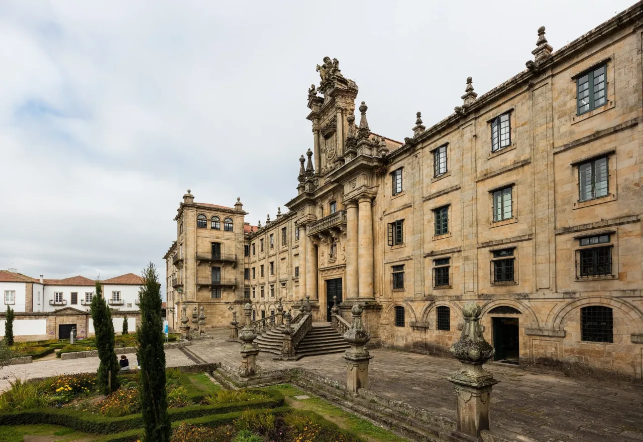 The long granite facade of San Martiño Pinario in Santiago de Compostela, its central doorway raised above a double stair and framed by a carved Baroque altarpiece front.