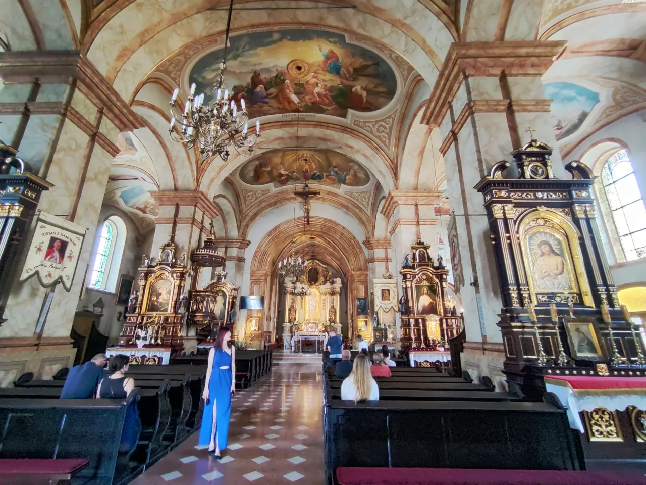 The nave of the Wadowice basilica looking east, painted vaults above whitewashed arcades, side altars along both walls and the high altar beyond the crossing.