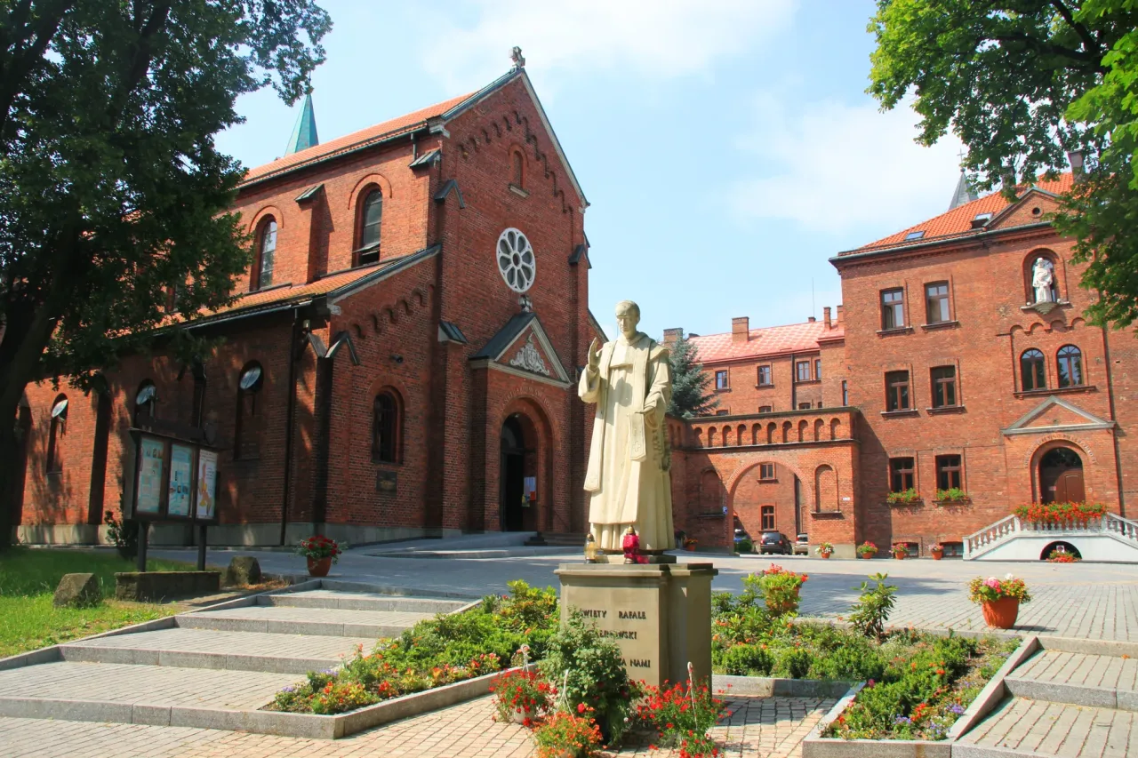 The Carmelite church and the brick monastery buildings beside it in Wadowice, a standing statue on a plinth in the garden between them.