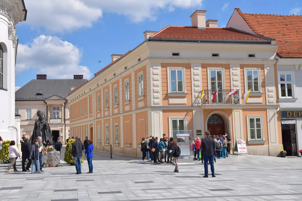 The ochre-fronted building of the John Paul II Family Home Museum in Wadowice, flags above its doorway and a queue of visitors waiting on the square outside.